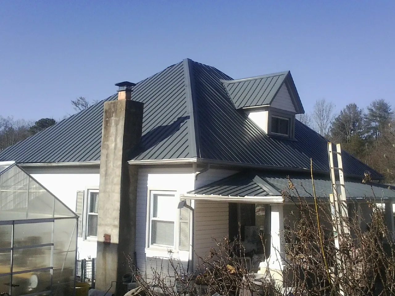 Dark blue standing seam metal roof on a white farmhouse with dormer — Slate & Tile Roof Repair by Roofing Brothers in Veteran