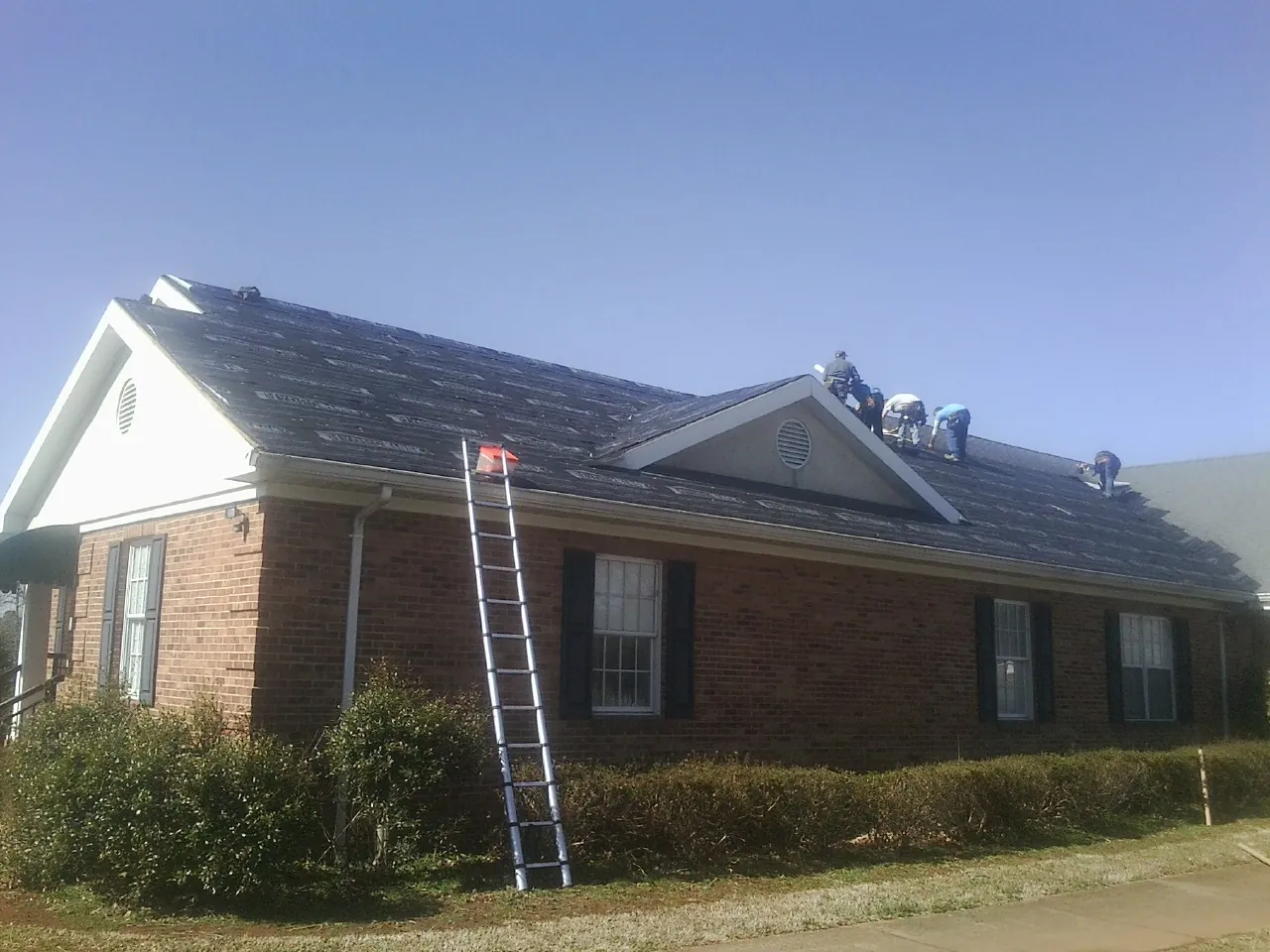 Crew tearing shingles off a brick ranch roof with a ladder set — Metal Roof Repair work by our crew in Veteran