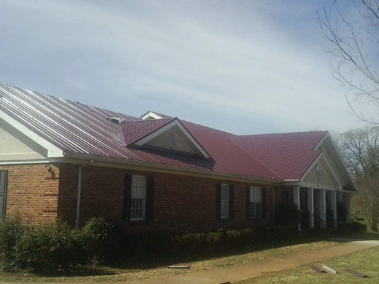 Red metal roof with gabled entries on a long brick building, from a Hail Damage Roof Repair job in Veteran