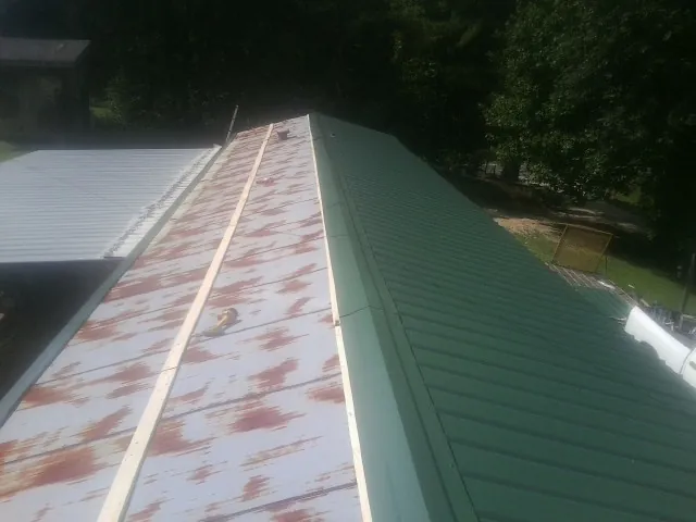Old rusted panels beside newly installed green metal roofing — Wind Damage Roof Repair by Roofing Brothers in Veteran