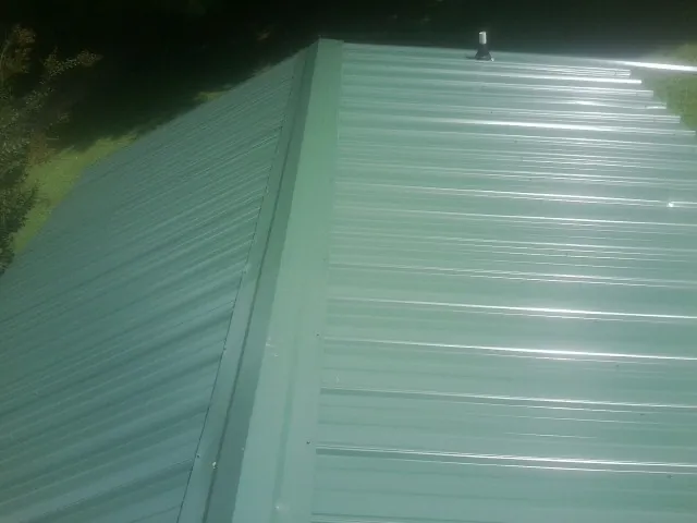 New green metal panels meeting at the ridge of a roof — Flat Roof Repair work by our crew in Veteran