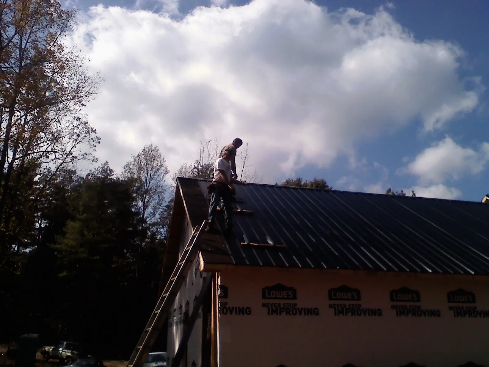 Roofer fastening dark metal panels high against a cloudy sky, from a Roof Inspection job in Veteran
