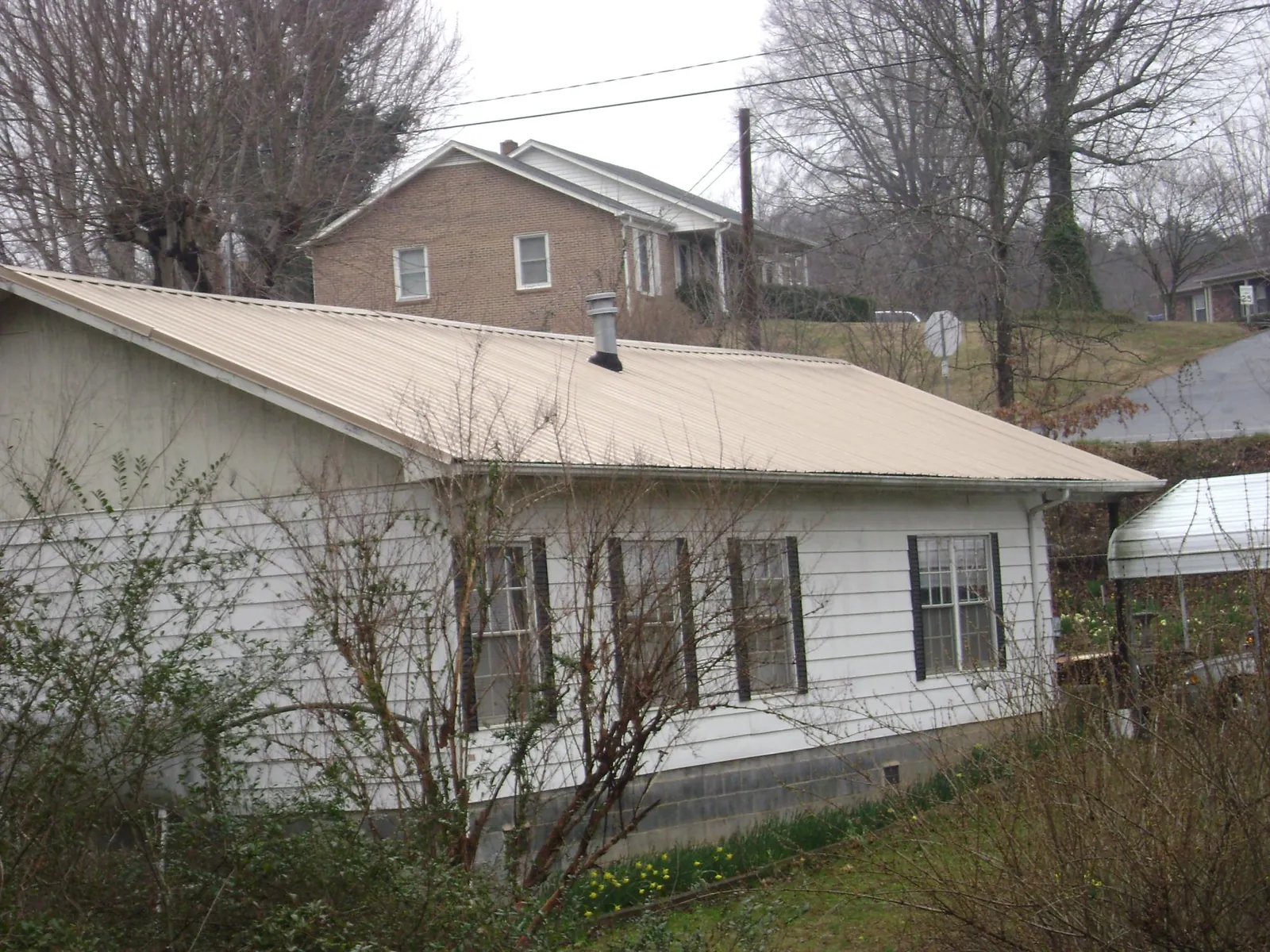 Tan metal roof on a white sided house set into a hillside — Commercial Roofing by Roofing Brothers in Veteran