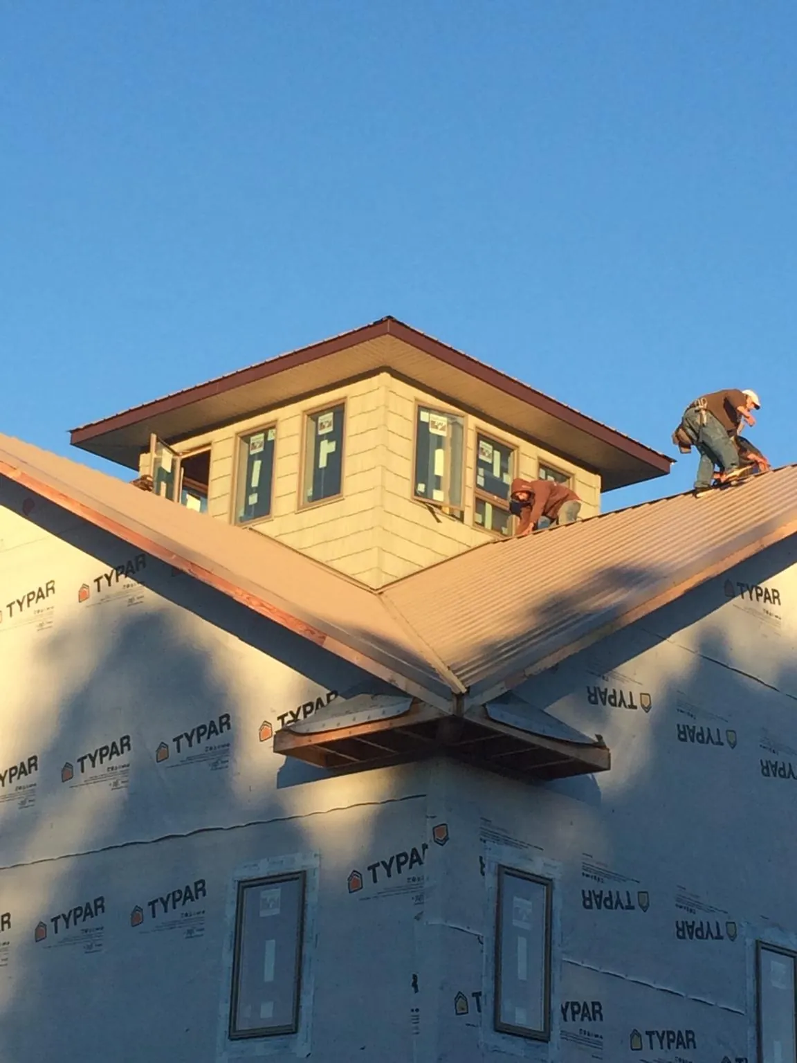 Roofers working around a rooftop cupola on a new metal roof at sunset — Roof Waterproofing in Veteran by Roofing Brothers